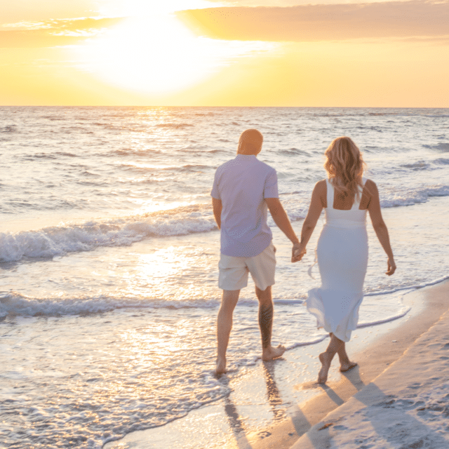 couple walking on the beach at sunset holding hands for a photography session in longboat key