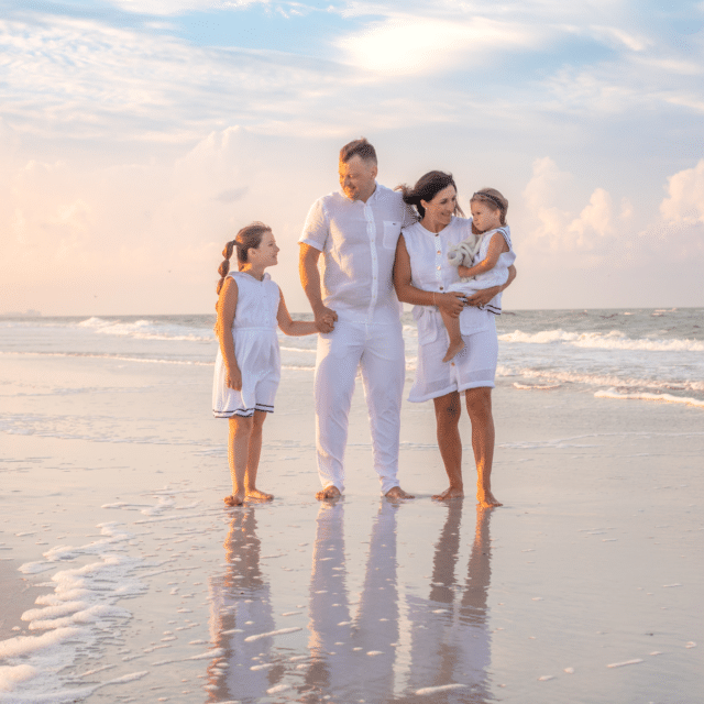 Family of four standing on siesta key beach at sunrise with a reflection in the sand