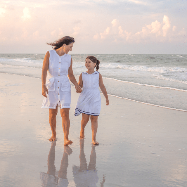 Mom and daughter walking on the beach and holding hands at sunrise in longboat key Florida photographed by Siesta Key family photographer Heather Hinson